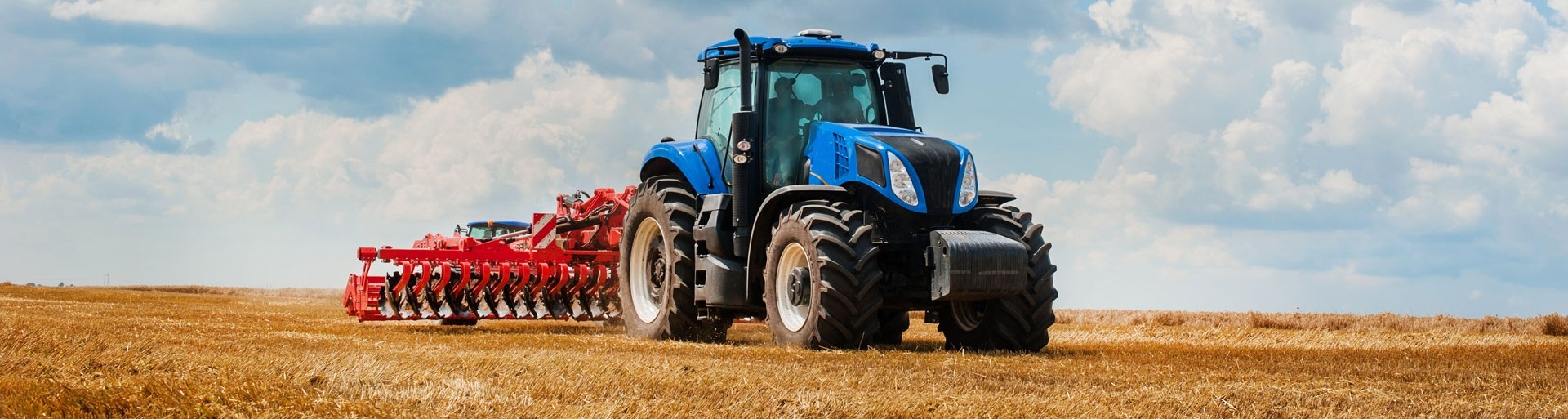 Een blauwe tractor is het land aan het omploegen met een mooie lucht op de achtergrond